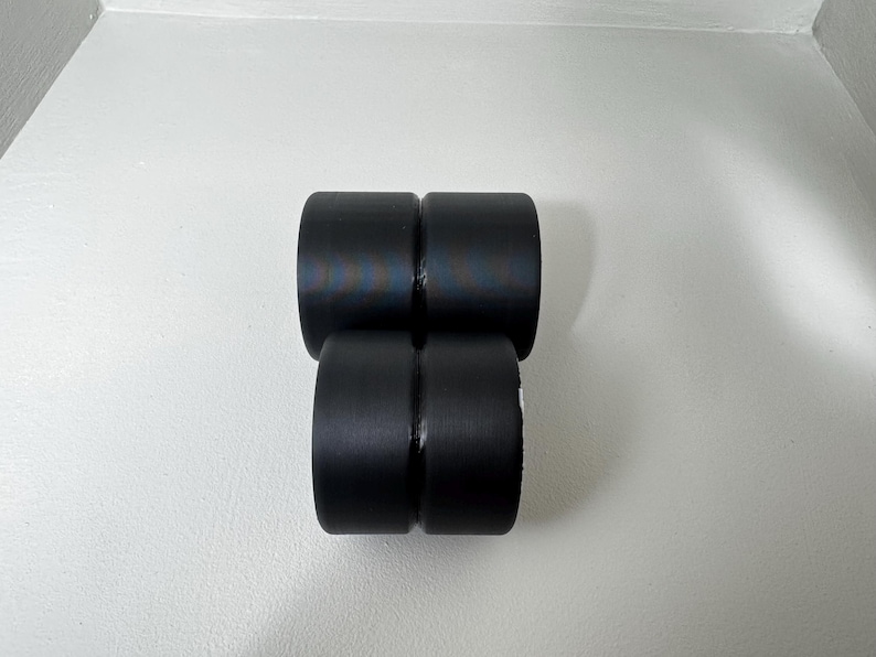 May include: Four black cylindrical objects are stacked in a rectangular formation. The objects have a smooth, matte finish and appear to be made of a solid material. The objects are arranged against a white background.