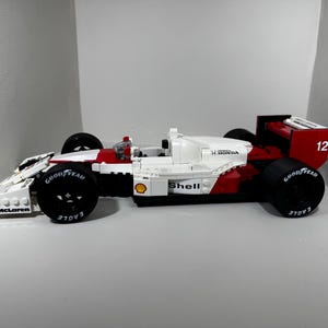 May include: A white, red, and black race car model with Goodyear tires. The model has the Shell and H. Honda logos. The number 12 is visible on the rear wing. The car is a McLaren model.
