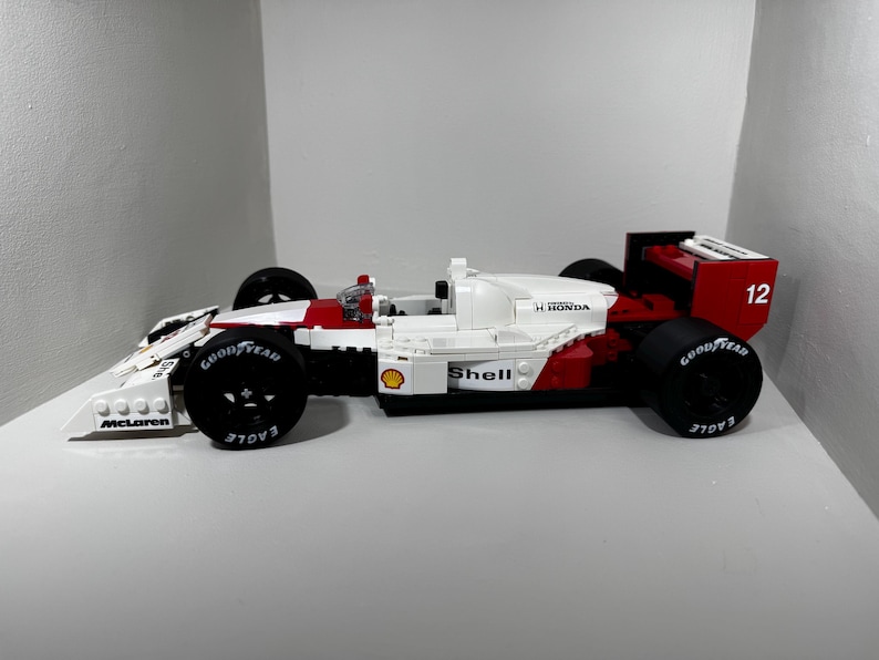 May include: A white, red, and black race car model with Goodyear tires. The model has the Shell and H. Honda logos. The number 12 is visible on the rear wing. The car is a McLaren model.