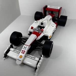May include: A white and red race car model with black tires. The car has the number 12 and the Shell logo. The car is a replica of a Honda McLaren Formula 1 car.
