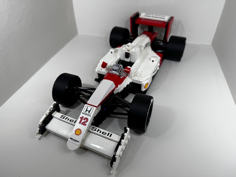 May include: A white and red race car model with black tires. The car has the number 12 and the Shell logo. The car is a replica of a Honda McLaren Formula 1 car.