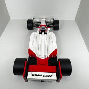 May include: A white, red, and black toy race car with large black tires. The car has the word "McLaren" printed on the front. The top of the car has the word "Shell" printed on it.