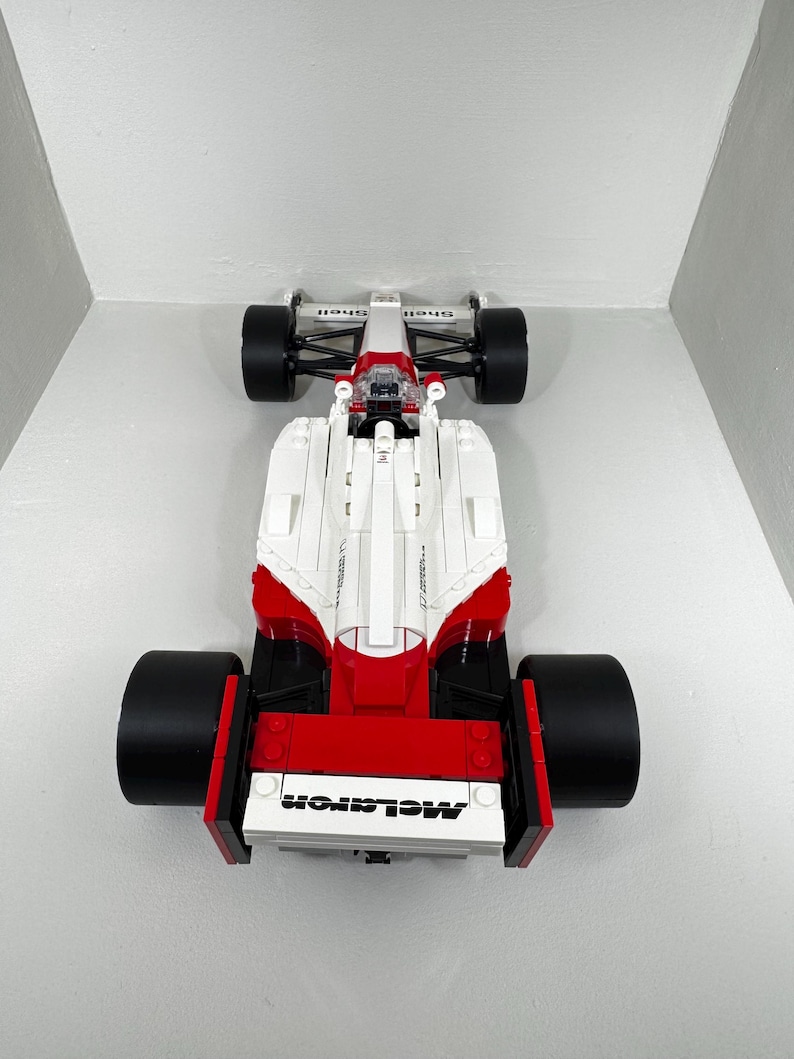 May include: A white, red, and black toy race car with large black tires. The car has the word "McLaren" printed on the front. The top of the car has the word "Shell" printed on it.