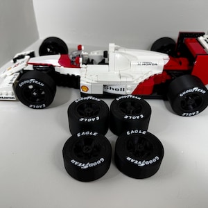 May include: A white, red, and black race car model with four black tires. The car has the number 12 on the side and the Shell and Honda logos. The tires have the Goodyear and Eagle logos.