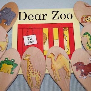 May include: A collection of wooden spoons, each decorated with a hand-painted animal: elephant, lion, frog, giraffe, camel, dog, monkey, and snake. The book "Dear Zoo" is visible, with a sign saying "From the Zoo".