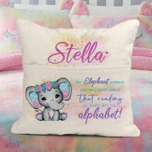 Pode incluir: Uma almofada personalizada com um elefante de desenho animado fofo e o texto "Stella, um elefante sabe e nunca esquecerá que a leitura começa com o alfabeto!"