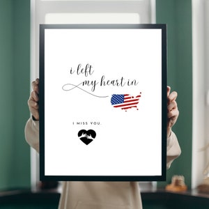 May include: A framed print with the text "i left my heart in" followed by an outline of the United States with the American flag inside. Below the map is the text "I miss you." and a black heart with two hands inside.