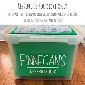 May include: A clear plastic file box with a green insert. The box has a white decal that reads "FINNEGAN'S KEEPSAKE BOX." The image also includes text that says "LISTING IS FOR DECAL ONLY" and "THIS IMAGE SHOWS YOU HOW THE DECAL WILL LOOK WHEN APPLIED TO A FILE BOX."