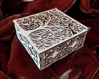 Op de afbeelding: Een witte houten doos met een decoratief, ingewikkeld, lasergesneden ontwerp van een boom met draaiende takken. De doos staat op een rood fluwelen oppervlak.