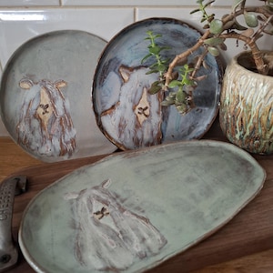 May include: Handmade ceramic plates and a serving platter with a sheep design. The plates are in shades of blue and green with a textured finish. The sheep design is in a contrasting colour, adding a unique touch to the tableware.