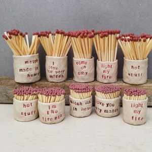 May include: Ten small ceramic matchstick holders with various romantic sayings, such as "match made in heaven", "I love you very match", "come on baby", "light my fire", and "hot stuff". Each holder is filled with wooden matchsticks with red tips.