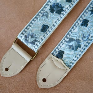 以下が含まれることがあります： ライトブルーと白の花柄刺繍が施されたギター用ストラップ2本。 ストラップはクリーム色の革の端と金色の金属製金具が付いています。 花柄は濃い青色の花と葉が特徴です。