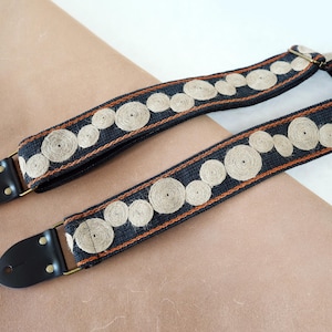 May include: A black guitar strap with brown and white embroidered circles.