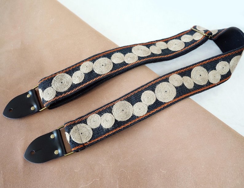 May include: A black guitar strap with brown and white embroidered circles.