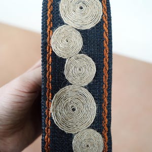 May include: A black fabric trim with a brown stitched border and a pattern of beige woven circles.