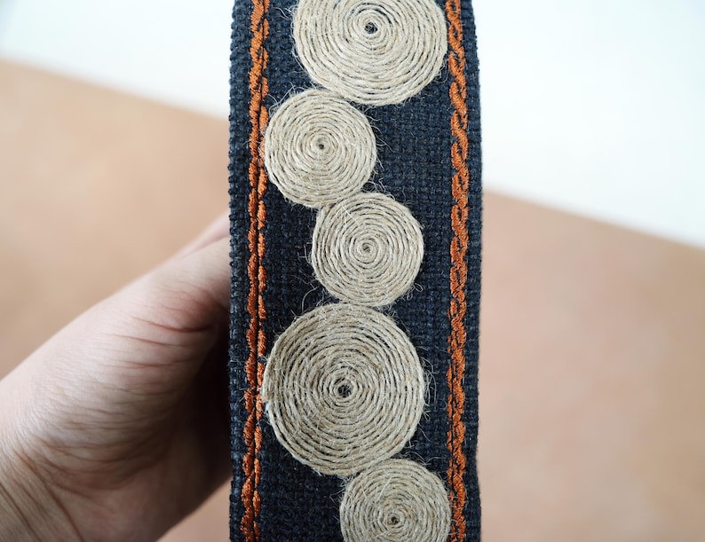 May include: A black fabric trim with a brown stitched border and a pattern of beige woven circles.
