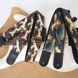 May include: Two guitar straps featuring a Japanese-inspired wave pattern. The left strap has black, white, and red waves, while the right strap displays black, white, and blue waves. Both have black leather ends and adjustable brass-toned hardware.