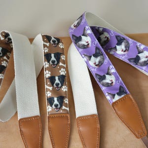May include: Three camera straps with dog and cat patterns. One strap is brown with dog faces, bones, and paw prints. Another is purple with cat faces and paw prints. All straps have white canvas and brown leather ends.