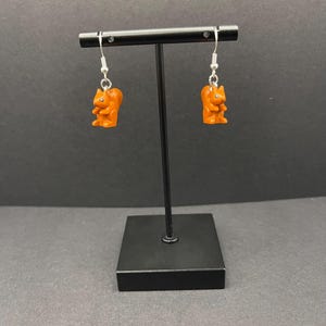 May include: A pair of dangle earrings featuring a brown squirrel charm on each earring. The earrings are hanging from a silver hook.