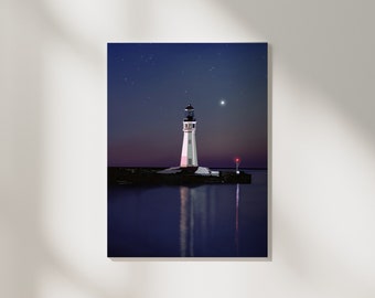 Puede incluir: Un faro blanco con techo negro se alza sobre una pequeña isla en un cuerpo de agua azul oscuro. El agua refleja la luz del faro y las estrellas en el cielo nocturno.
