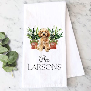 May include: White kitchen towel with a watercolor illustration of a light brown dog sitting between two potted plants. The text "The Larsons" is printed in black script below the dog.