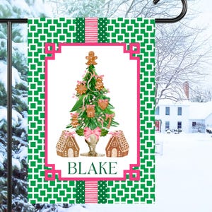 May include: A green and pink Christmas-themed garden flag with a gingerbread house and tree decorated with gingerbread ornaments. The flag has a white background with a pink border and the name "BLAKE" in pink letters.