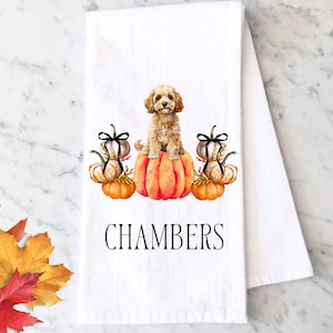 May include: White kitchen towel with a watercolor illustration of a dog sitting on a pumpkin, flanked by pumpkins with black bows. The word "CHAMBERS" is printed below the pumpkins. Autumn leaves are in the corner.
