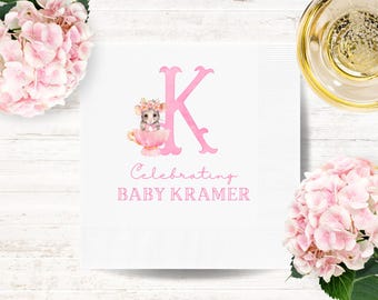 May include: White square paper napkin with a pink floral design and the text "Celebrating BABY KRAMER". The design includes a pink letter "K" and a watercolor illustration of a mouse in a teacup. Pink hydrangeas and a glass of champagne are in the background.
