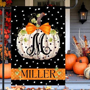 May include: A black and white polka dot garden flag featuring a white pumpkin with a large orange bow and the letter "M". The word "MILLER" is displayed in orange. Pumpkins and fall foliage decorate the porch.