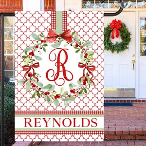 May include: A red and green Christmas wreath with a white background and the letter "R" in the center. The wreath is surrounded by a red and white checkered pattern. The text "REYNOLDS" is at the bottom of the wreath.