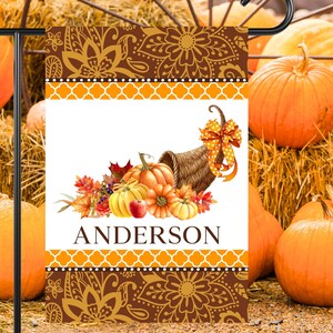 May include: A personalized fall-themed garden flag with a cornucopia overflowing with pumpkins, gourds, and fall leaves. The flag has a brown and gold paisley pattern with a white background and the name "Anderson" printed in black.