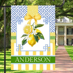 May include: A yellow and blue garden flag with a lemon motif and the name "Anderson" printed on the bottom. The flag has a geometric pattern and a yellow bow.