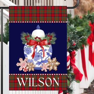 May include: A blue and white porcelain ginger jar with a red bow and green pine sprigs. The jar is surrounded by gingerbread cookies with red and white candy canes. The background is a dark blue with a red and green plaid border. The text "WILSON" is printed in white at the bottom of the flag.