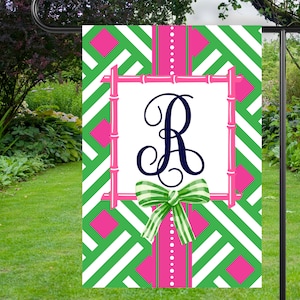 May include: A green and pink garden flag with a white background and a bamboo frame. The flag features a large, white letter "R" in a navy blue font with a green and white bow. The flag is designed with a chevron pattern.