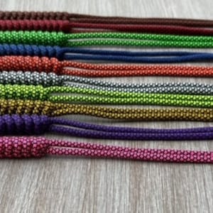 May include: A set of 10 colorful paracord keychains with a variety of colors including brown, green, blue, red, silver, gold, and purple. Each keychain has a black metal clip.