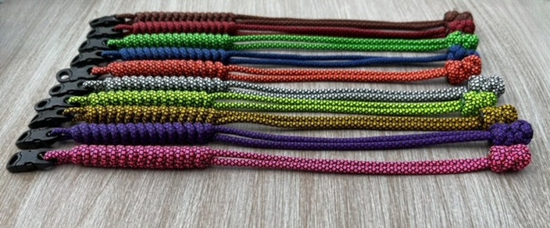 May include: A set of 10 colorful paracord keychains with a variety of colors including brown, green, blue, red, silver, gold, and purple. Each keychain has a black metal clip.