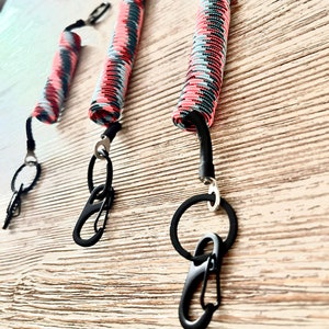 Puede incluir: Tres llaveros negros con cordones en espiral de colores y clips metálicos negros. Los cordones son una mezcla de rosa, azul y negro.