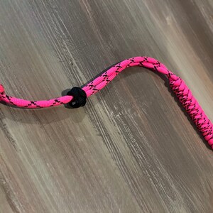 May include: A pink and black paracord lanyard with a knot at one end and a metal clip at the other.