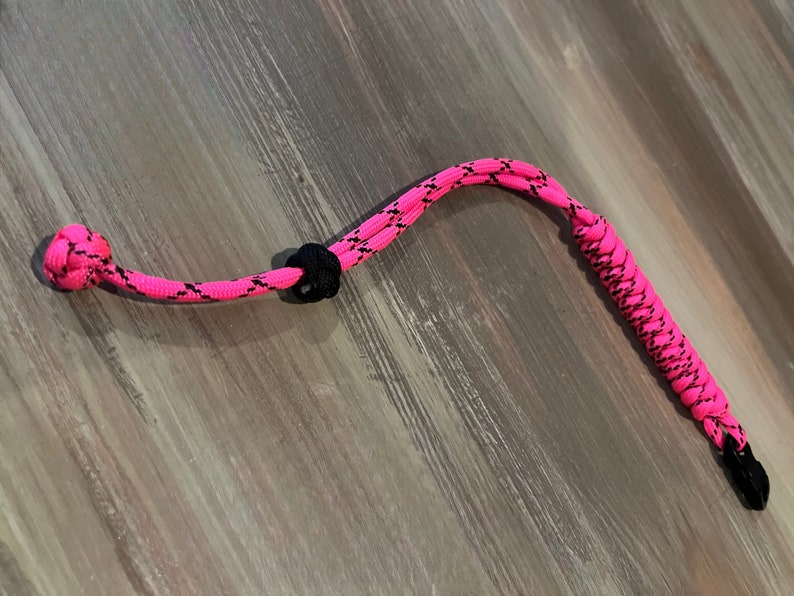 May include: A pink and black paracord lanyard with a knot at one end and a metal clip at the other.