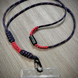 Puede incluir: Un cord&oacute;n negro y rojo con un clip negro y un porta credenciales de pl&aacute;stico transparente.