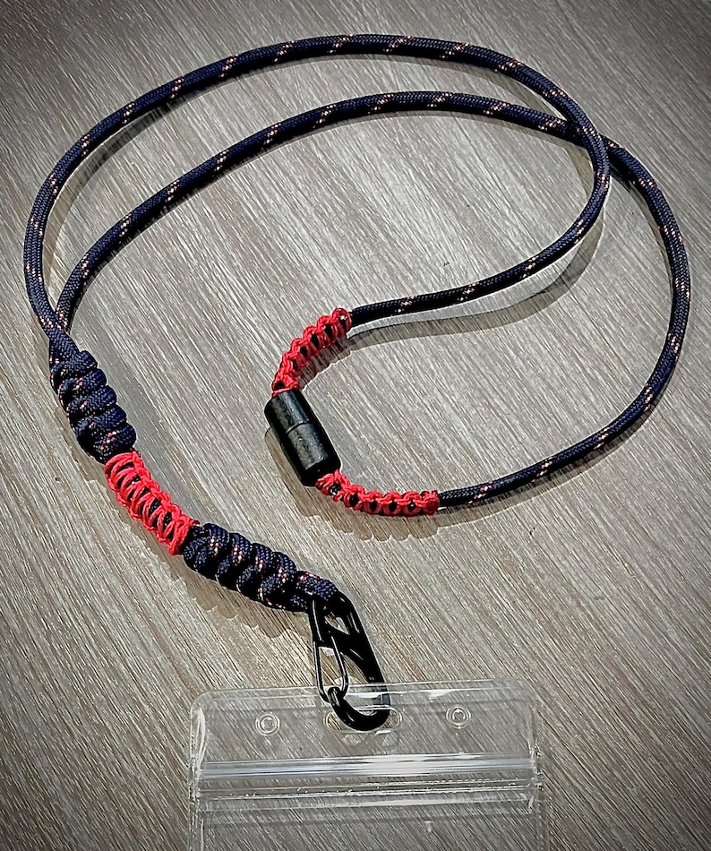 Puede incluir: Un cord&oacute;n negro y rojo con un clip negro y un porta credenciales de pl&aacute;stico transparente.
