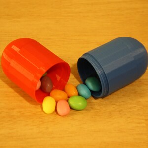 May include: A red and blue pill-shaped container with a variety of colorful candy spilling out.