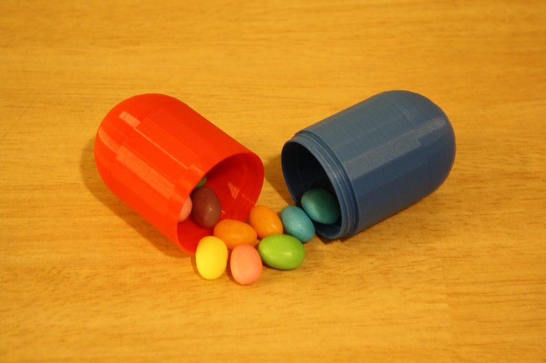 May include: A red and blue pill-shaped container with a variety of colorful candy spilling out.