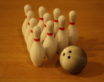 May include: A set of ten white bowling pins with red stripes, arranged in a triangle formation, with a gray bowling ball in front of them.