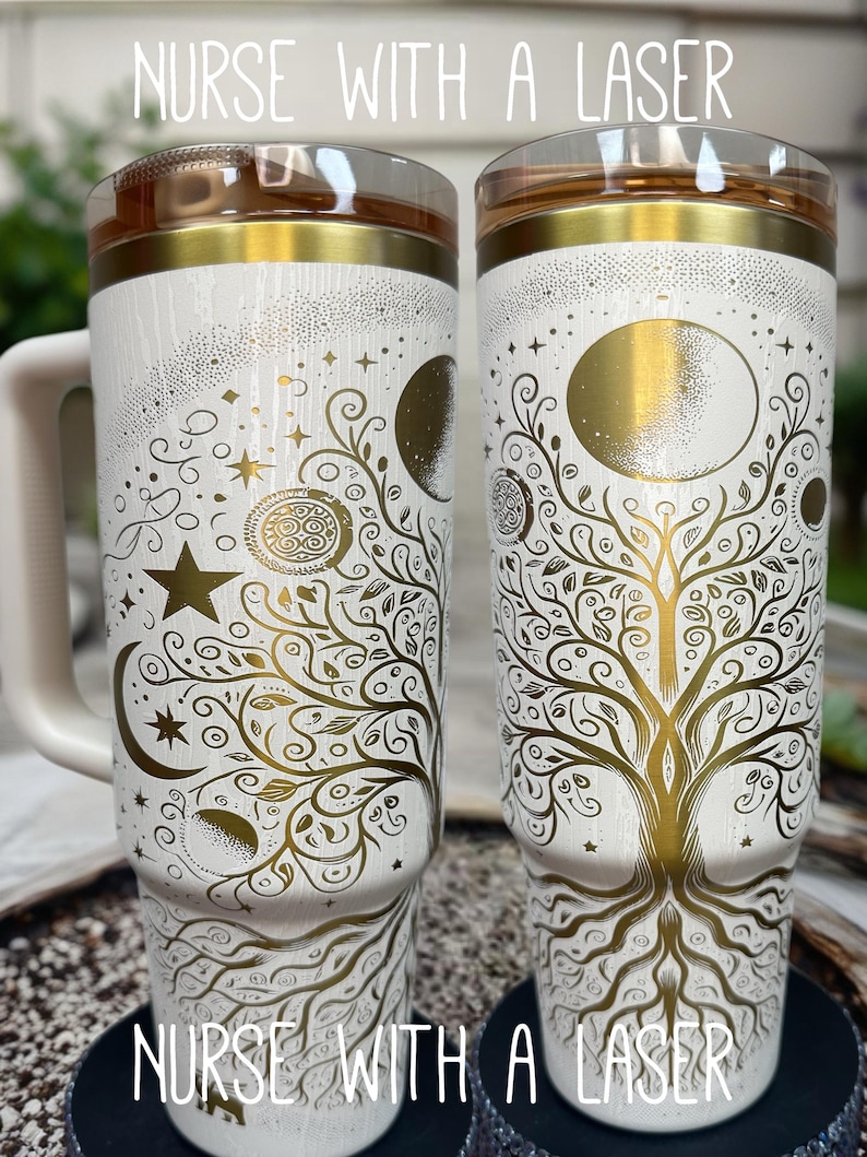 May include: Two white insulated tumblers with gold celestial and tree of life designs. The tumblers have a handle and a clear lid with a gold rim. The text "NURSE WITH A LASER" is printed on the top and bottom of the tumblers.