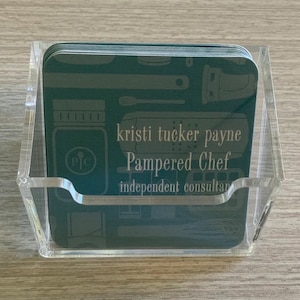Puede incluir: Un tarjetero de acr&iacute;lico transparente que contiene varias tarjetas de visita de color verde azulado. Las tarjetas presentan ilustraciones de utensilios de cocina y el texto "kristi tucker payne Pampered Chef independent consultant."