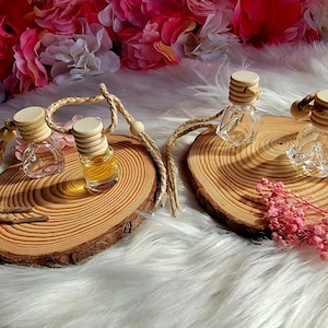 Peut inclure: Trois flacons en verre avec des bouchons en bois et des cordons suspendus sur des rondins de bois. Les flacons sont remplis d'un liquide clair. Les flacons sont sur une surface blanche et duveteuse.