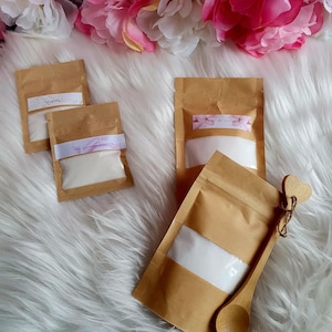 以下が含まれることがあります： 白い粉が入った小さな茶色の紙袋が3つ。それぞれの袋には、「アーモンド」、「ジャスミンフラワー」、「チェリーフラワー」という異なる名前のラベルが付いています。白い粉が入った大きな茶色の紙袋と、ハート型の柄のついた木製のスプーンがあります。