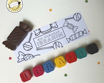May include: A white card with the text "Eid Mubarak Ibrahim" and a candy theme. The card is surrounded by colorful crayons that spell out the name "Ibrahim".