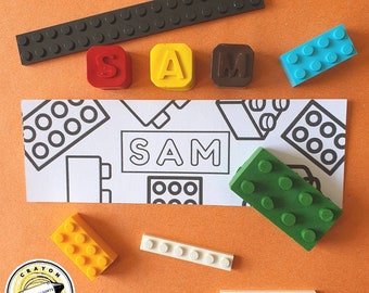 May include: An orange background displays a collection of colorful crayon blocks and a paper with the name "SAM". The blocks are in red, yellow, and brown, spelling out the name. Additional blocks are in blue, green, yellow, and white. A long, dark gray block is at the top.